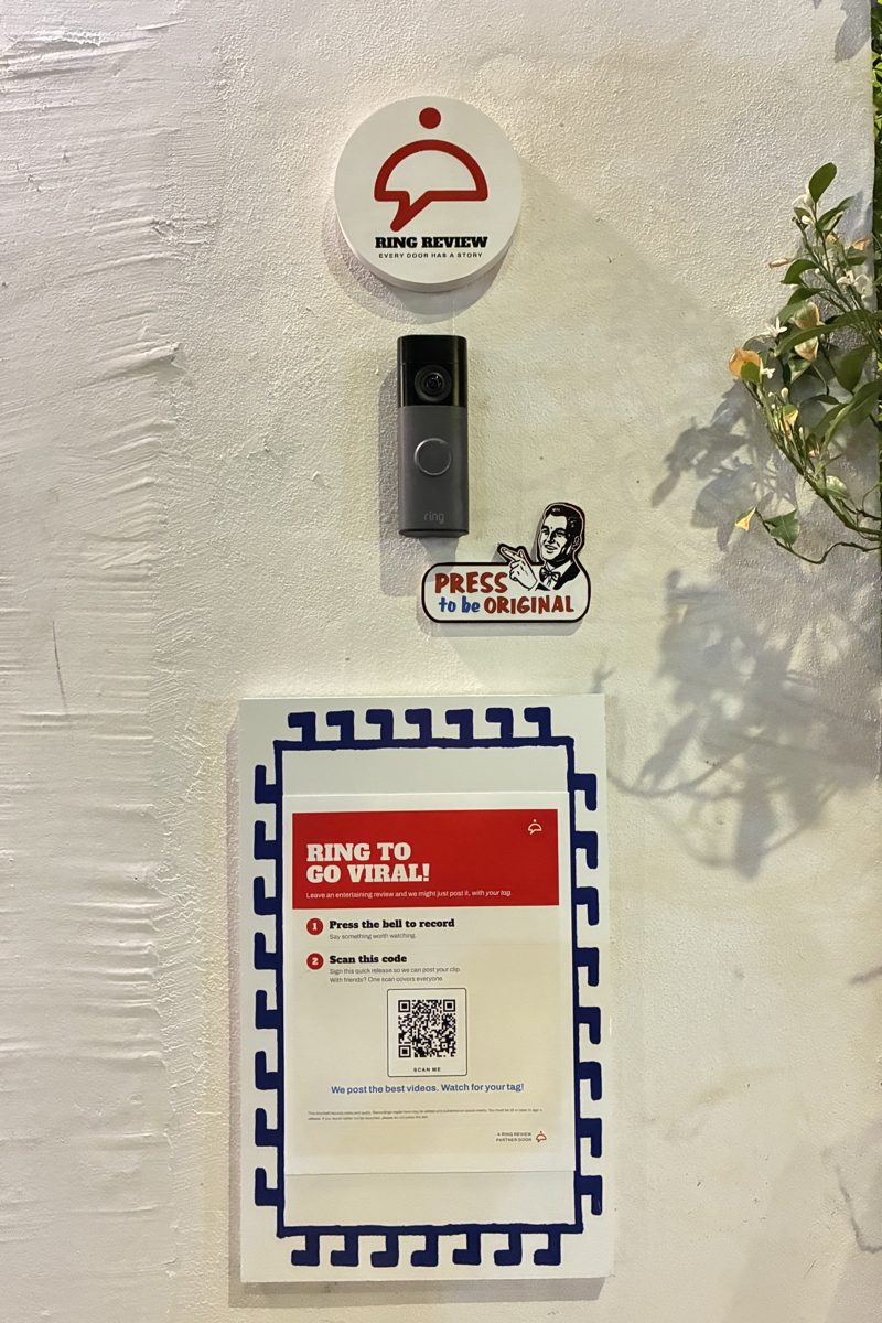The Ring Review setup on the wall at Tziki: the logo disc, the doorbell camera and the door sign with its QR code